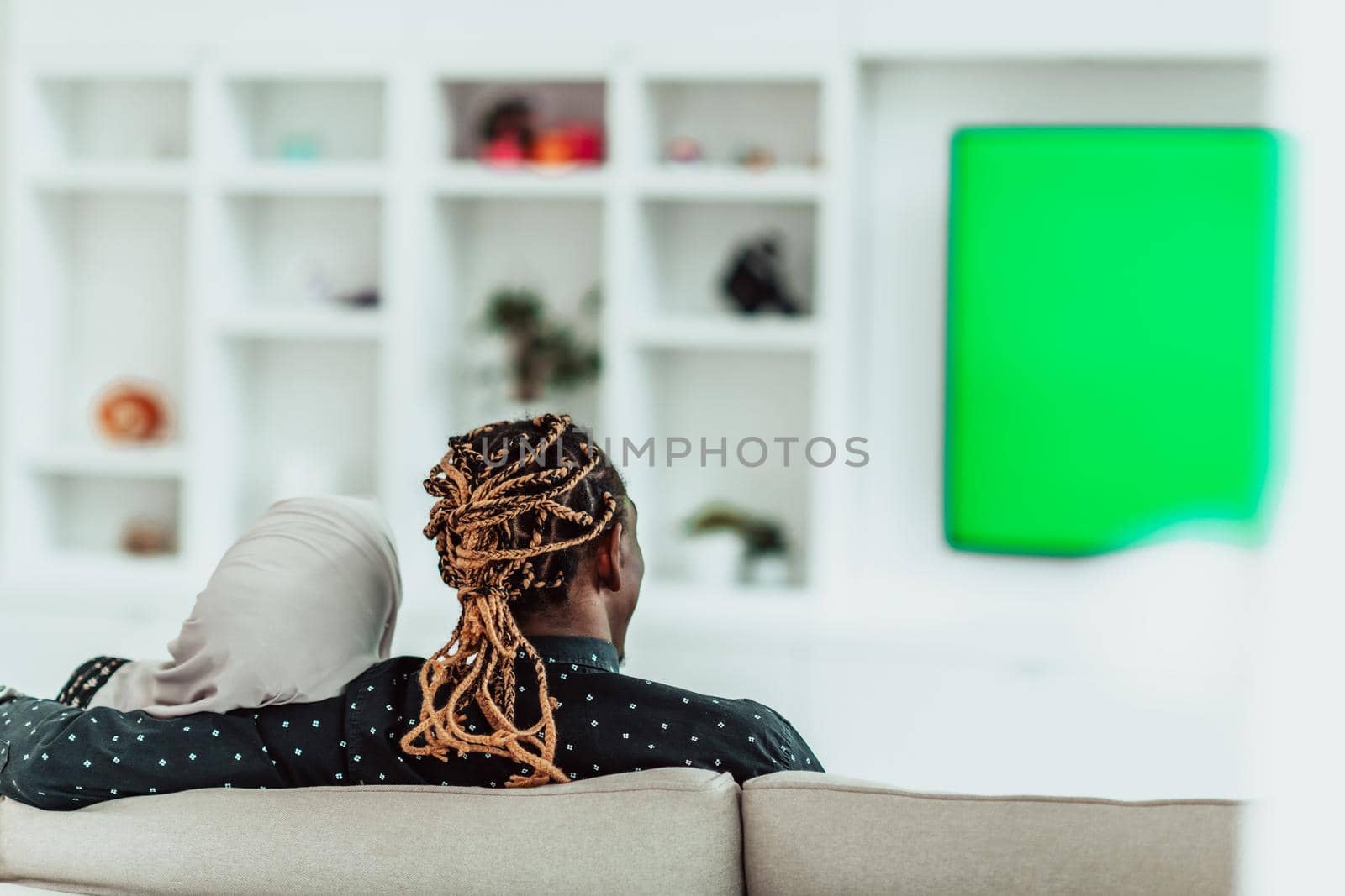 African Couple Sitting On Sofa Watching TV Together Chroma Green Screen Woman Wearing Islamic Hijab Clothes. High quality photo
