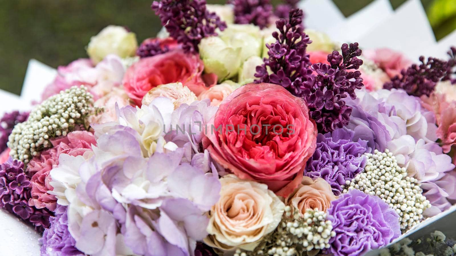 Wedding bouquet made of tree pink peony, purple carnations, blue hydrangea, lilac, wrapped in the craft paper