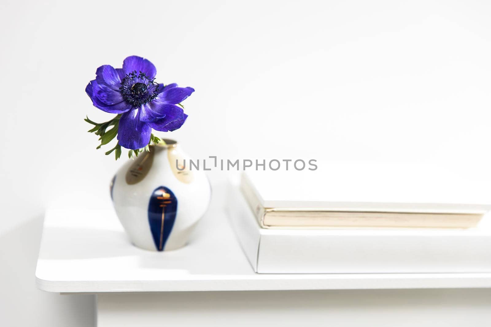 One blue anemone in a multi-colored vase in the style of the seventies on the table with books as an interior decoration. Copy space