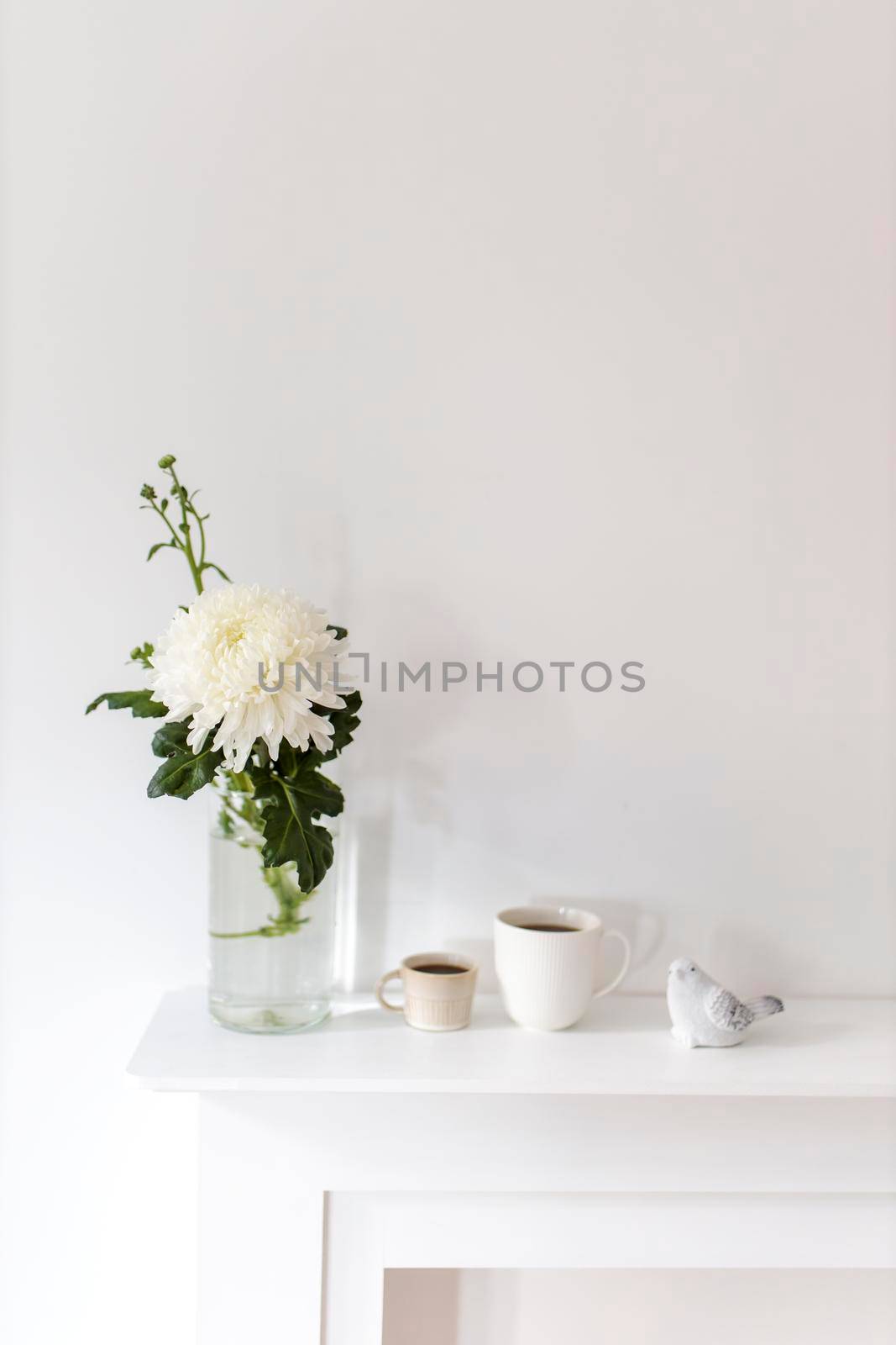 A large chrysanthemum in a glass vase, two fluted cups of coffee and ceramic bird figurines on the table. Office decoration. by elenarostunova