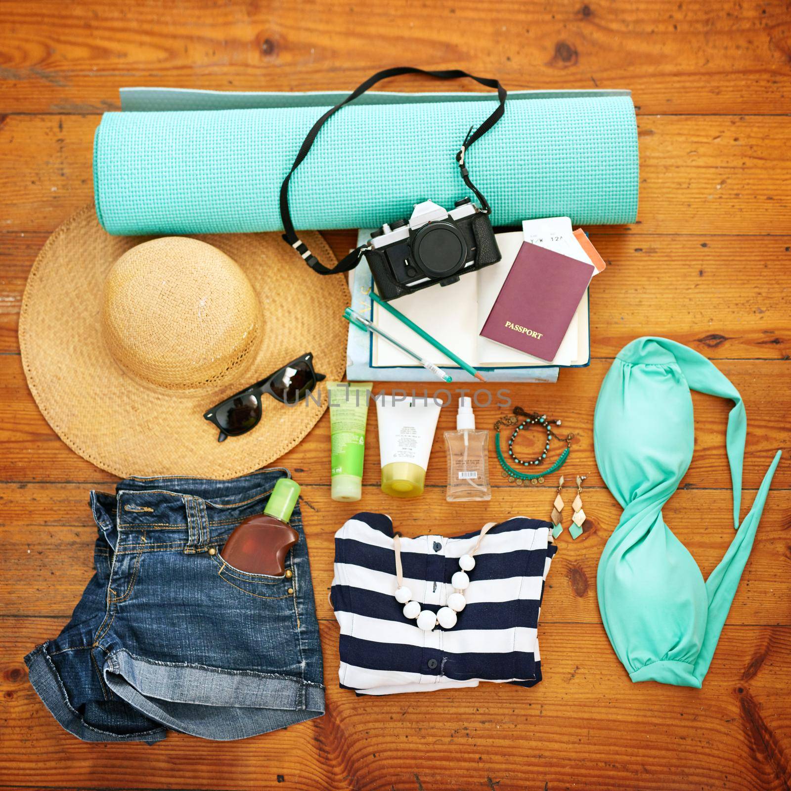 High angle shot of beachwear and travel paraphernalia arranged on a wooden floor.