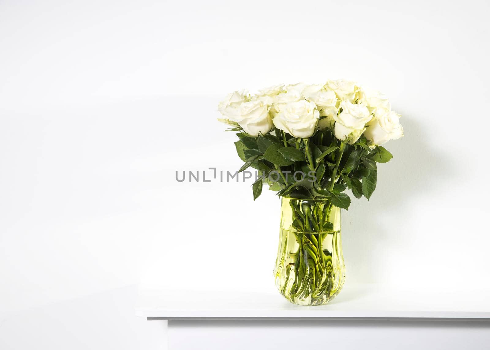 A bouquet of white roses in a vintage green glass vase on a white panel of a fake fireplace.