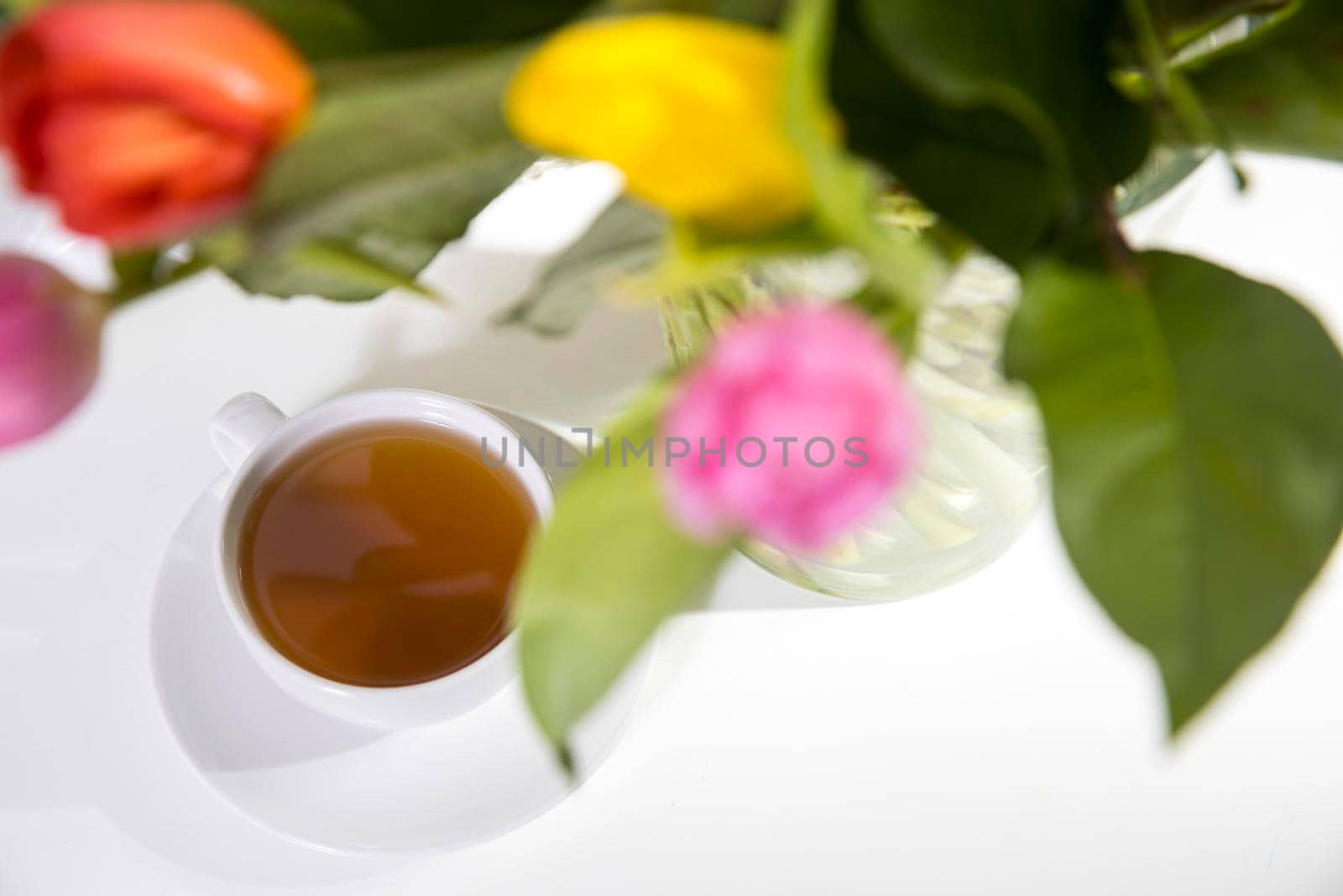 A bouquet of multi-colored tulips in a transparent vase and cup of tea by elenarostunova