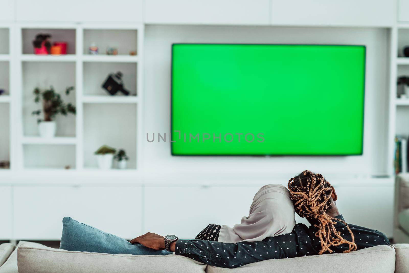 African Couple Sitting On Sofa Watching TV Together Chroma Green Screen Woman Wearing Islamic Hijab Clothes. High quality photo