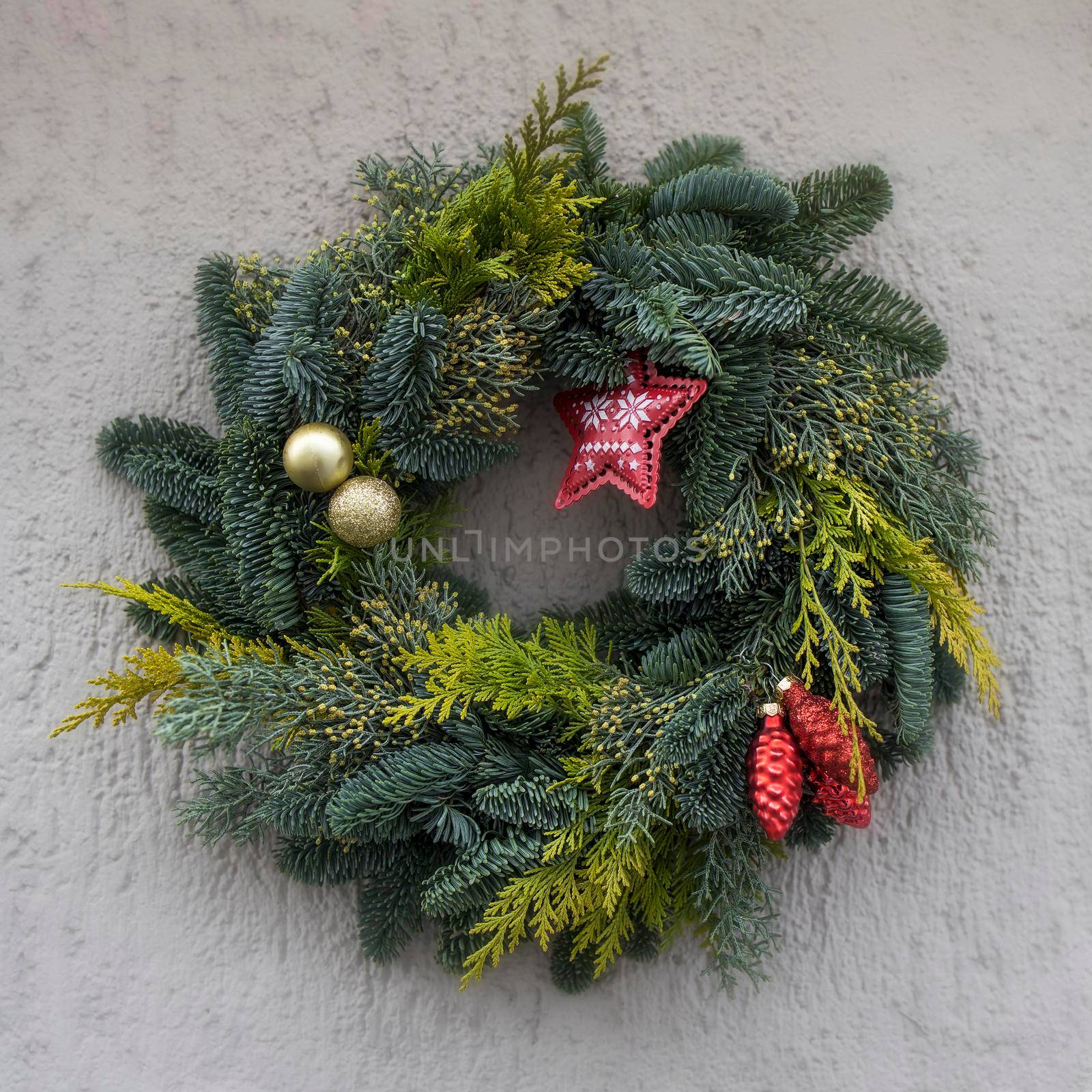 Christmas wreath of fir branches with decorations, star, balls hanging on grey wall of the house by elenarostunova