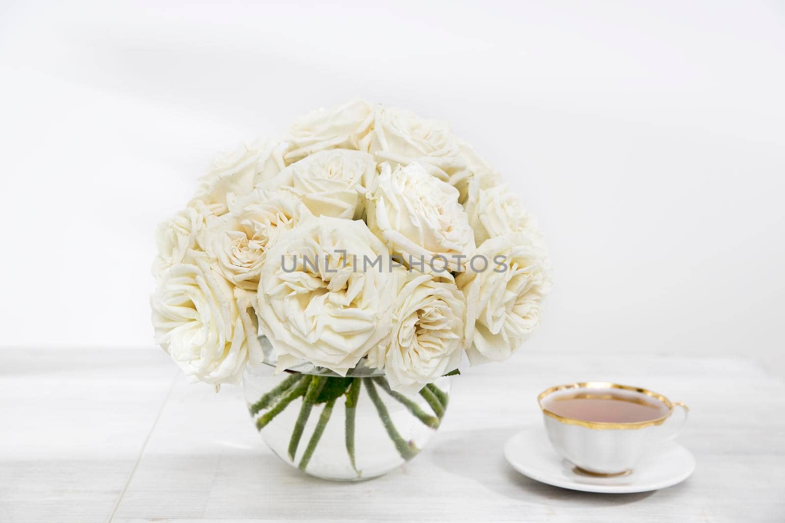 A bouquet of white roses in a glass vase on a table with cups of tea on the table. Copy space