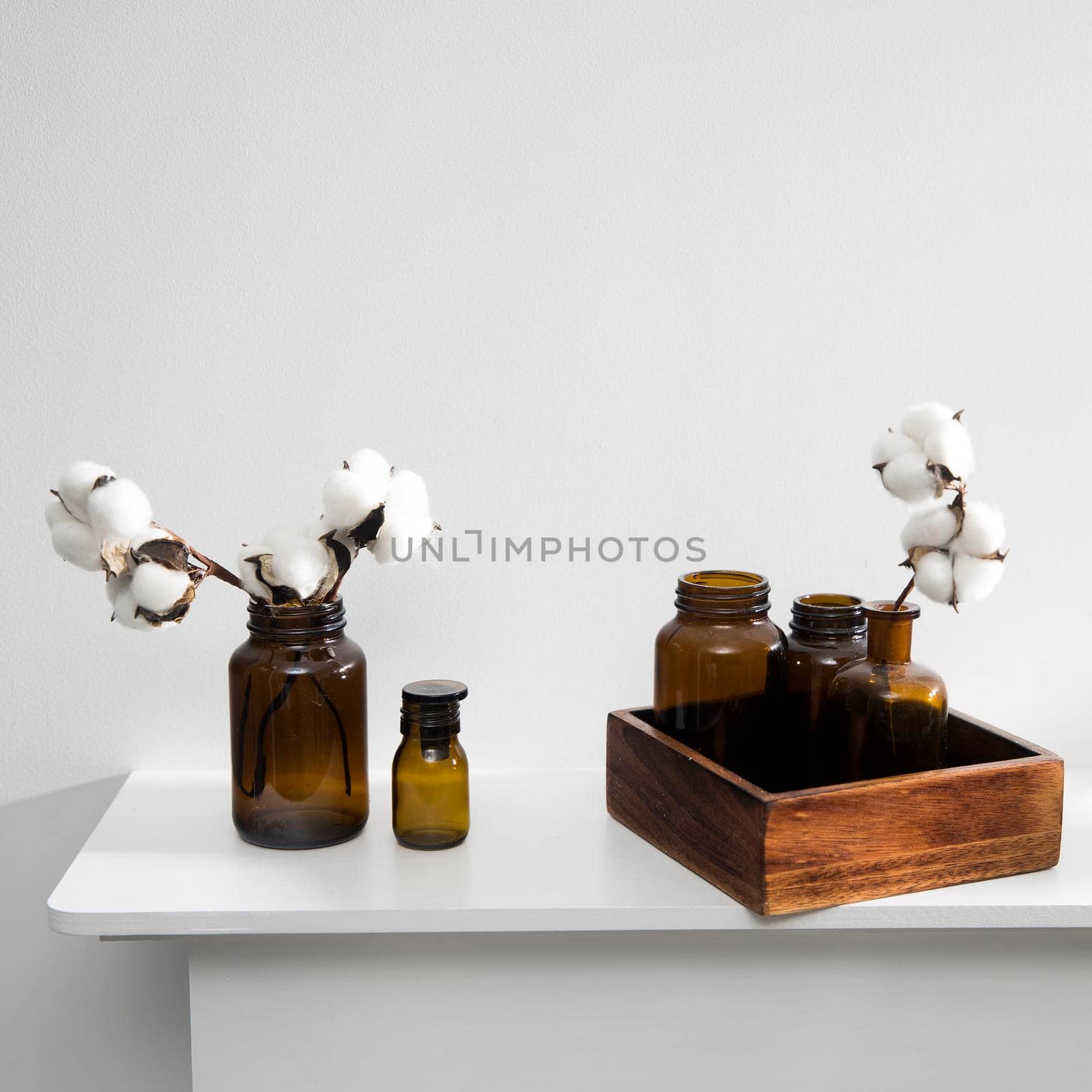 Cotton flowers in glass brown small pharmaceutical bottles on white table surface as room decoration. Copy space