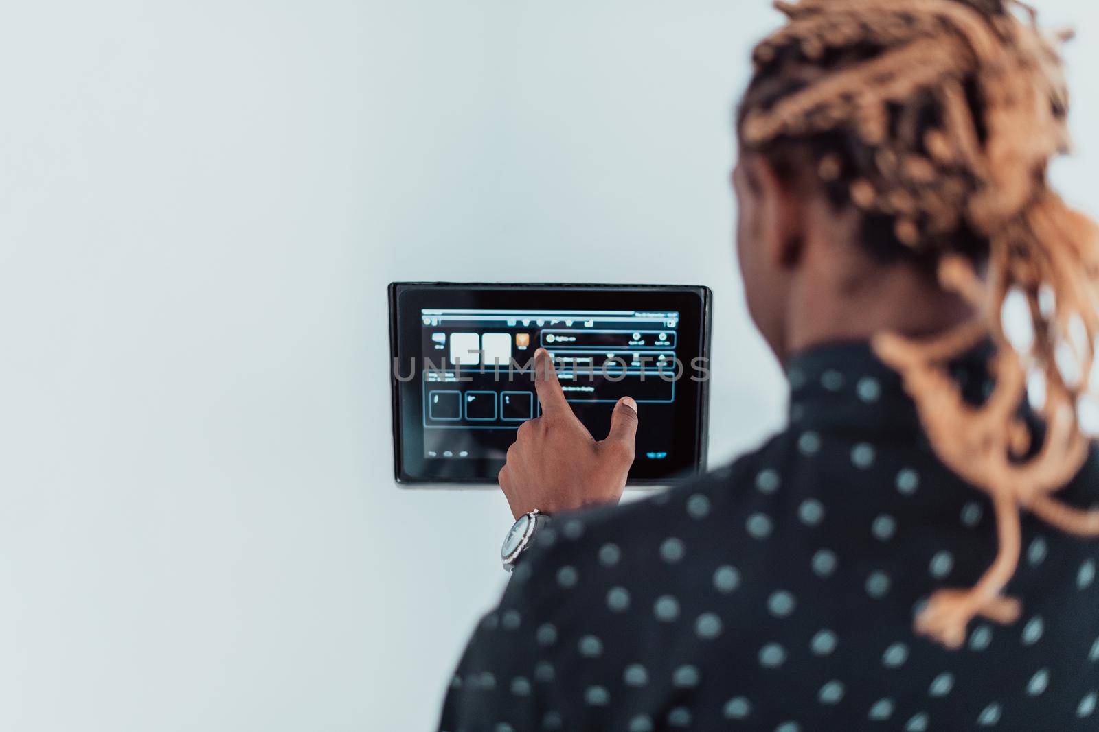 Smiling African American man using modern smart home system, controller on wall, positive young man switching temperature on thermostat or activating security alarm in apartment. High quality photo