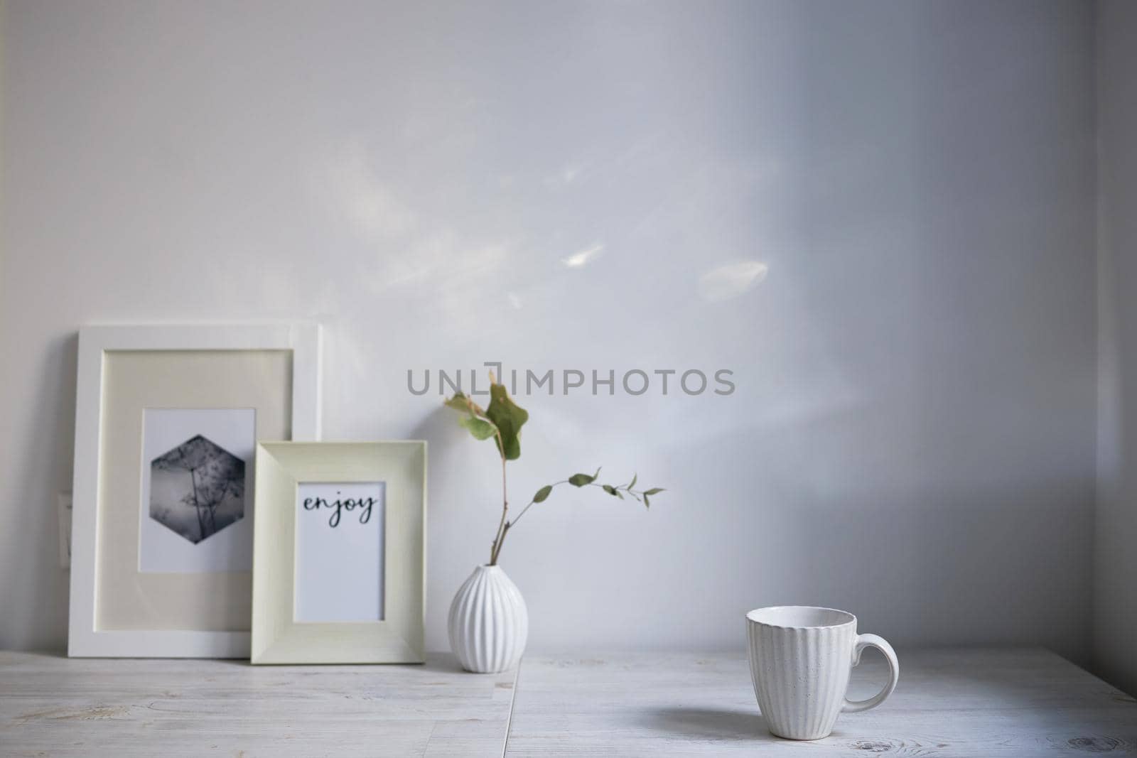 Scandinavian style. Interior Design. A white cup, a small vase with a dried eucalyptus branch, a two photo frames are on the table. Empty space for text by elenarostunova