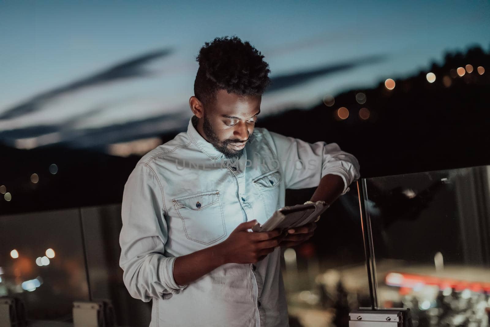 The young man on an urban city street at night texting on smartphone with bokeh and neon city lights in the background. by dotshock