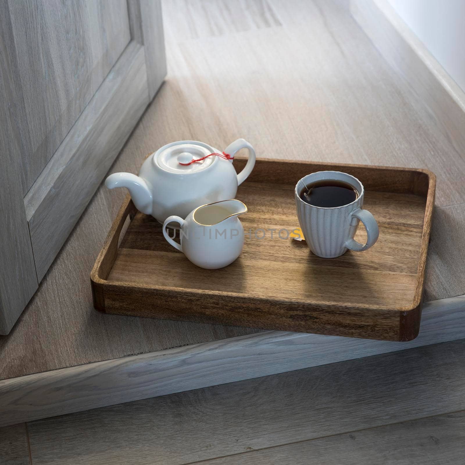A wooden tray with a cup of tea, a teapot, a milk jug is on the floor in the doorway. by elenarostunova