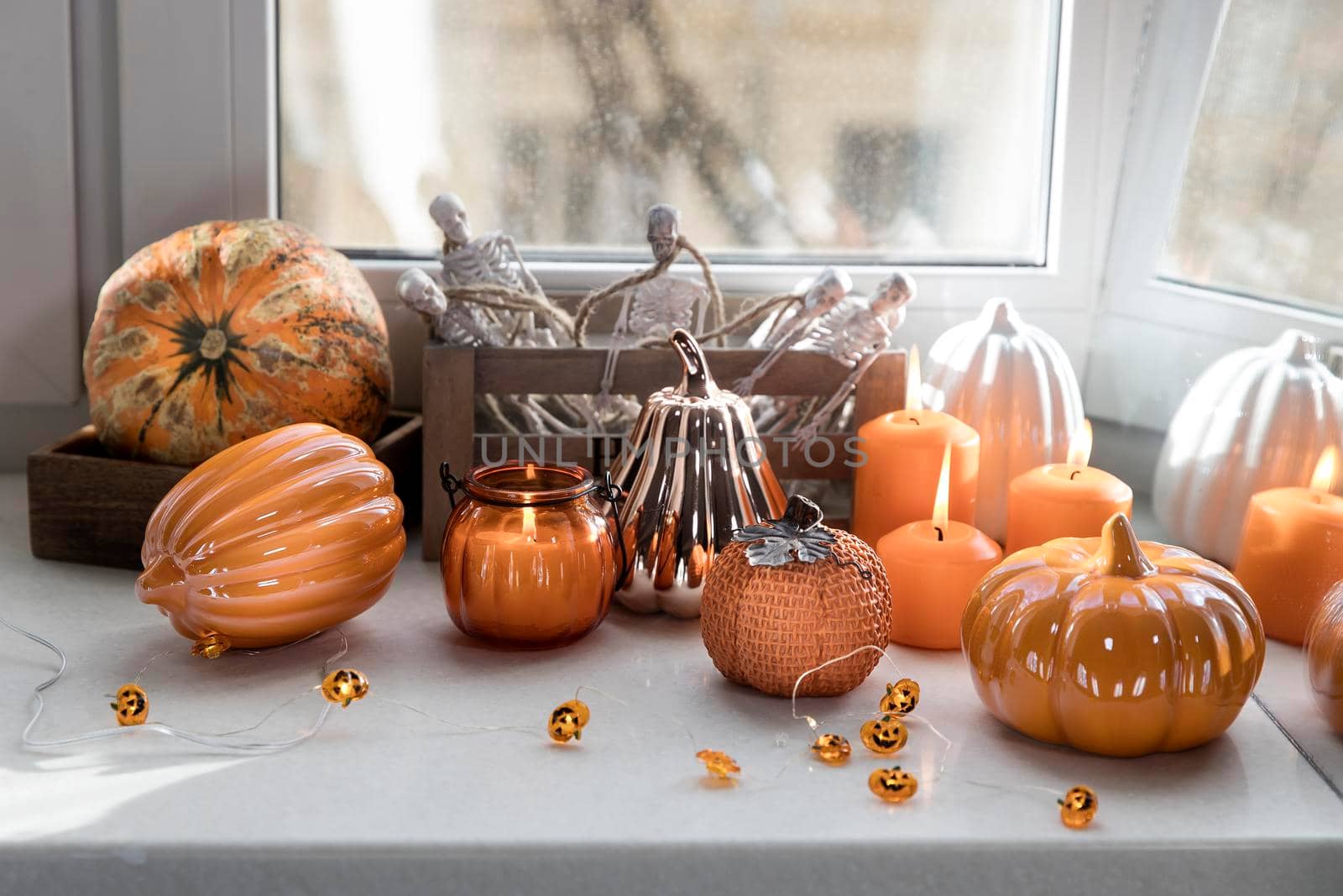 Porcelain and natural pumpkins, orange candles on a white table, Halloween decorations.