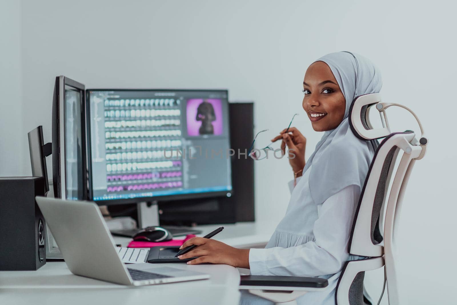 Young Afro-American modern Muslim businesswoman wearing a scarf in a creative bright office workplace with a big screen. High-quality photo