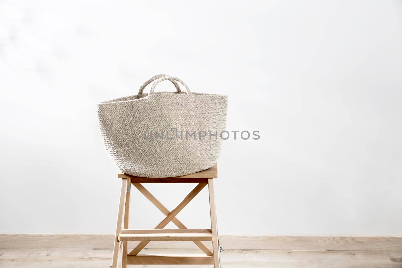 Large gray beach bag from canvas on a beige stool against a white wall. Place for text