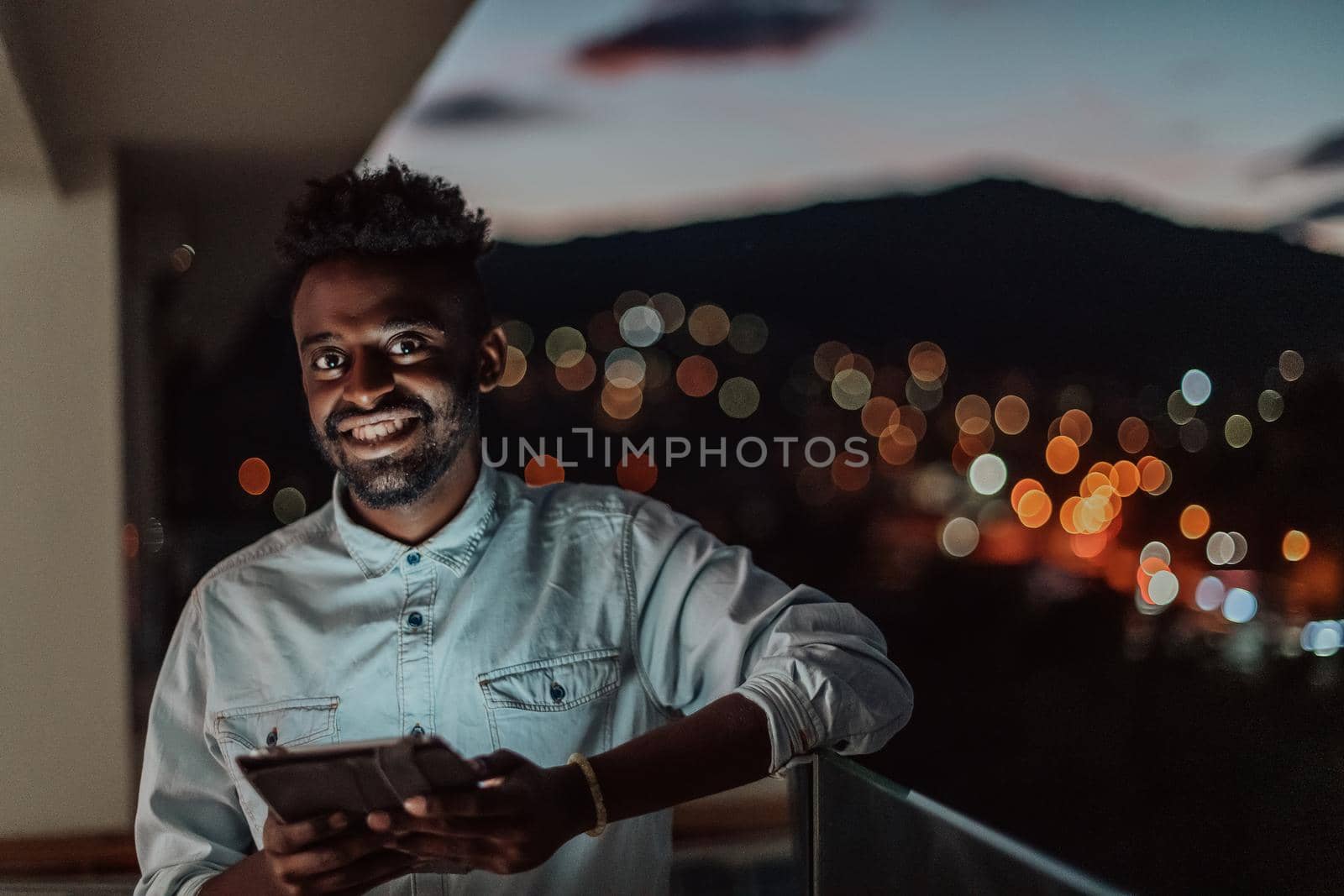 The young man on an urban city street at night texting on smartphone with bokeh and neon city lights in the background. by dotshock