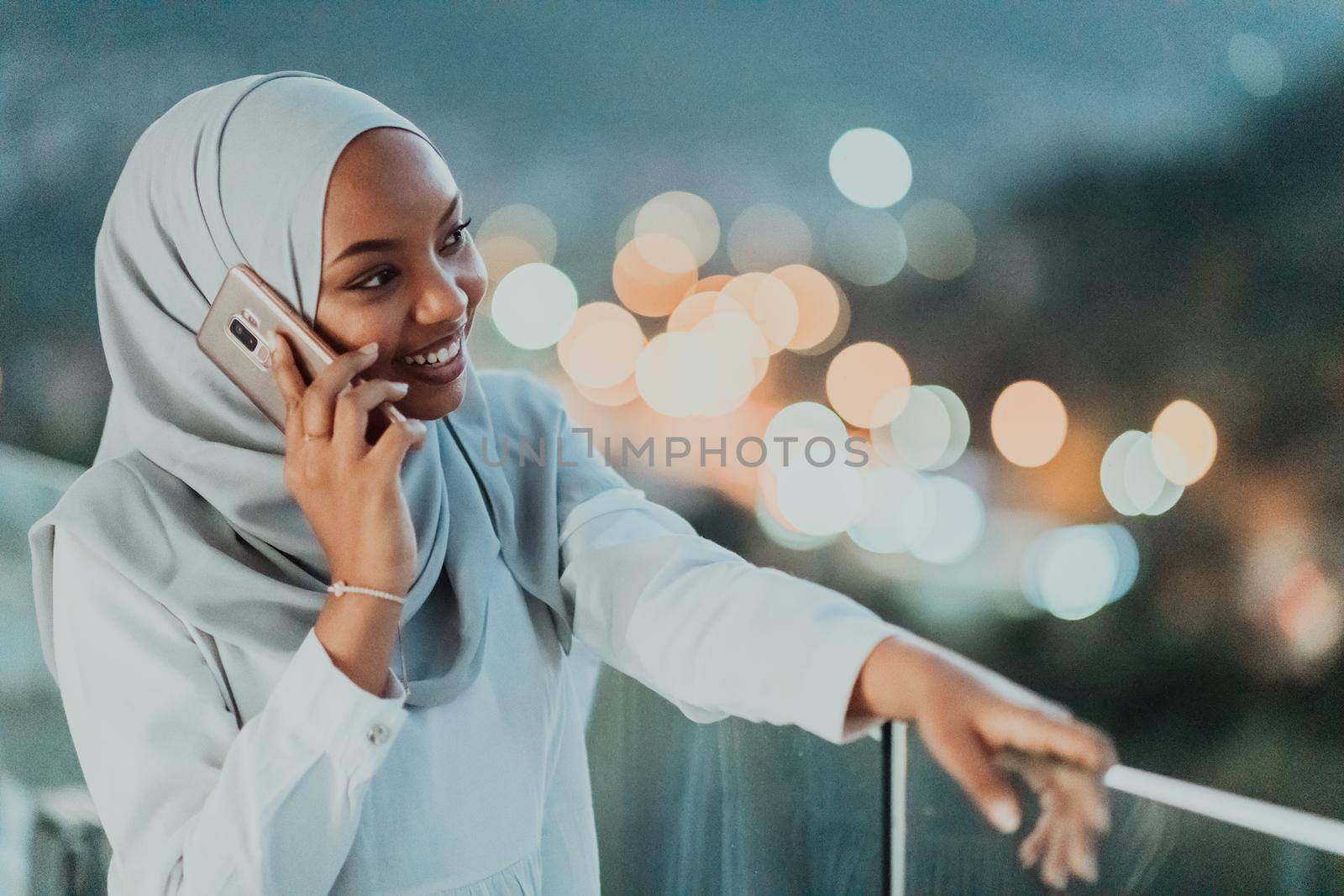 Young Muslim woman wearing scarf veil on urban city street at night texting on a smartphone with bokeh city light in the background. High-quality photo