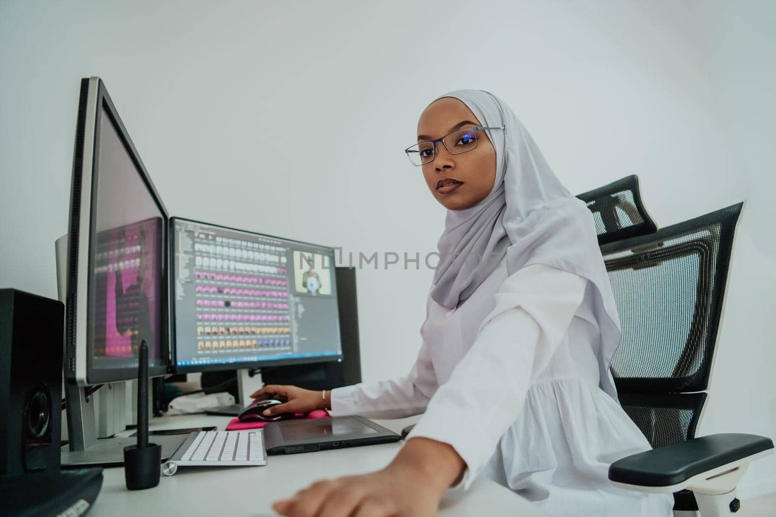 Young Afro-American modern Muslim businesswoman wearing a scarf in a creative bright office workplace with a big screen. by dotshock