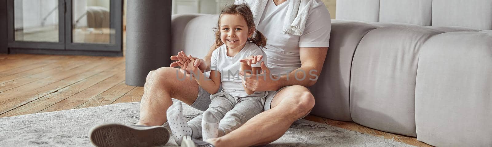 Full length portrait of joyful daughter sitting on floor with father while spending active day at home