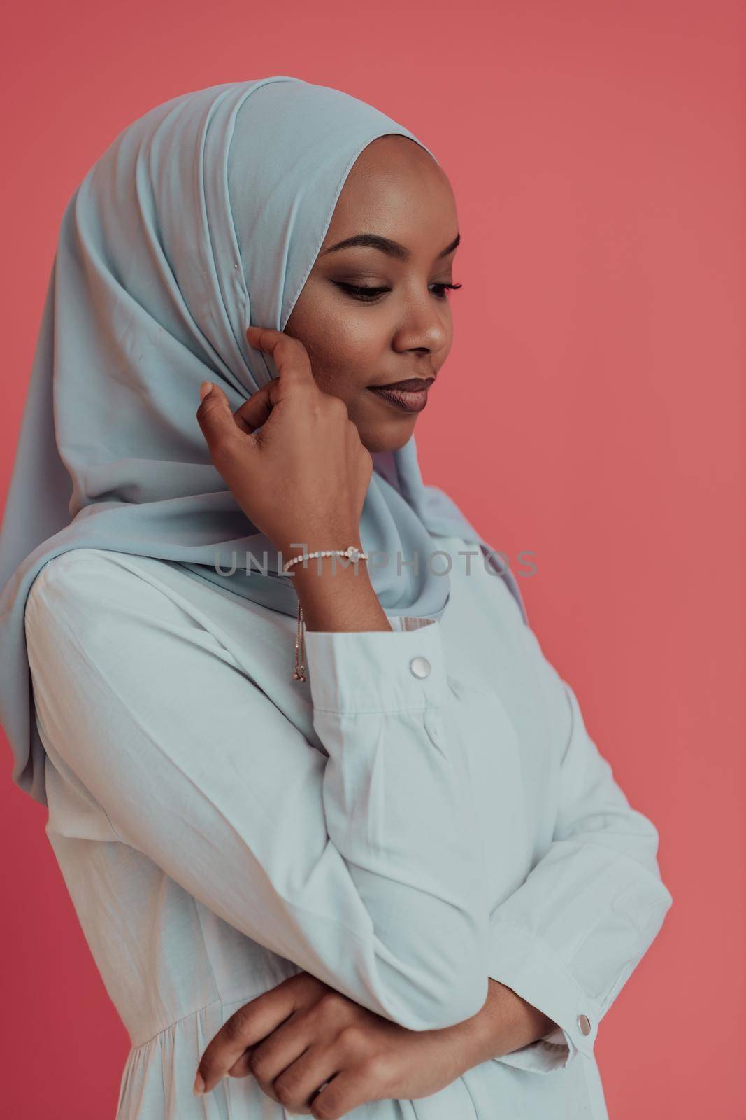 Portrait of young modern Muslim afro beauty wearing traditional Islamic clothes on plastic pink background. Selective focus. High-quality photo