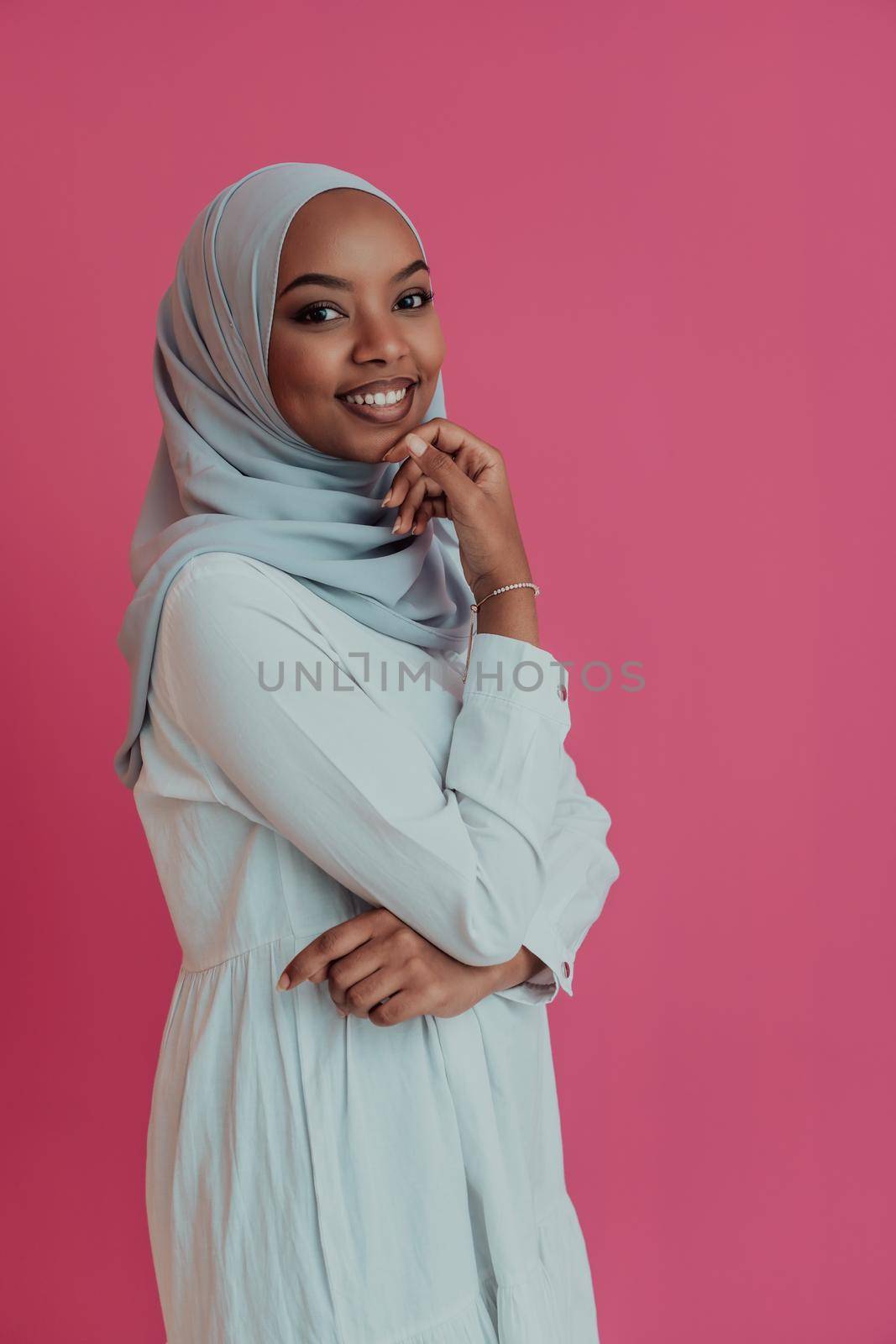 Portrait of young modern Muslim afro beauty wearing traditional Islamic clothes on plastic pink background. Selective focus. High-quality photo