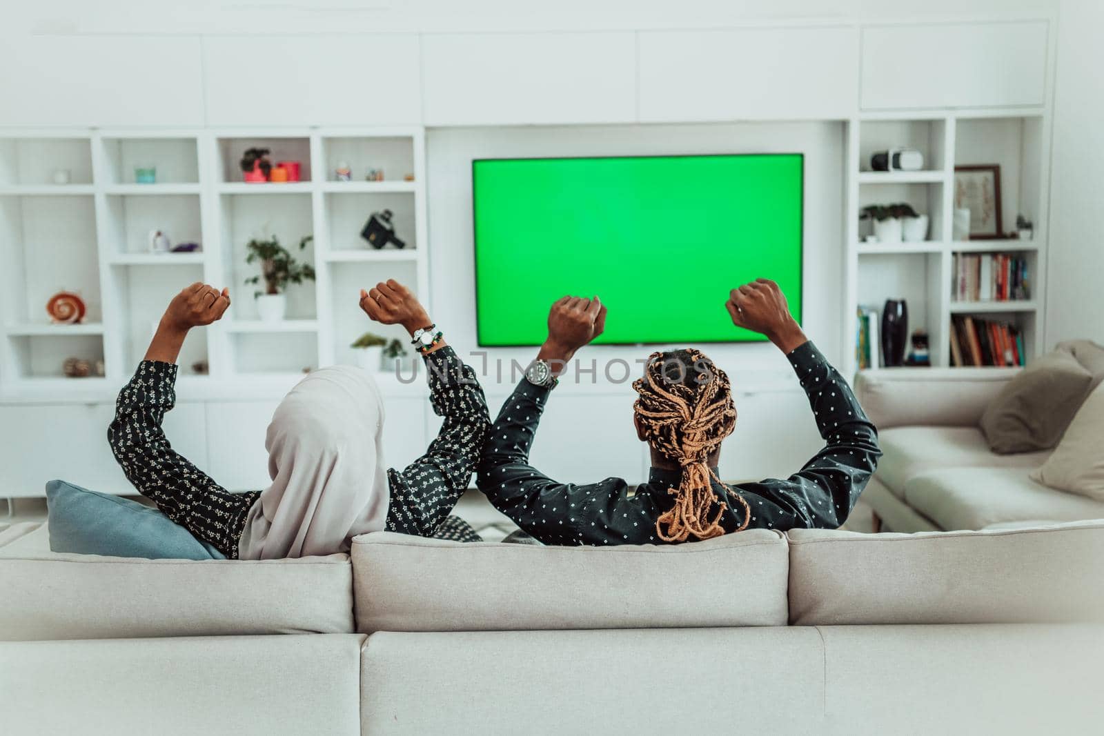 African Couple Sitting On Sofa Watching TV Together Chroma Green Screen Woman Wearing Islamic Hijab Clothes. High quality photo