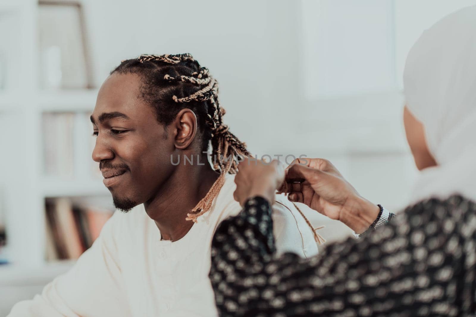 A young Muslim couple has a romantic time at home while the woman makes the hairstyle for her husband female wearing traditional Sudan Islamic hijab clothes. High-quality photo