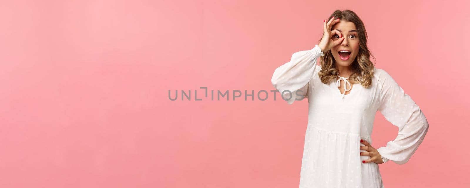 Portrait of amazed and fascinated, surprised young blond girl seeing something really cool, stare with excited and happy face, smiling found what looking for, look through okay sign over eye by Benzoix