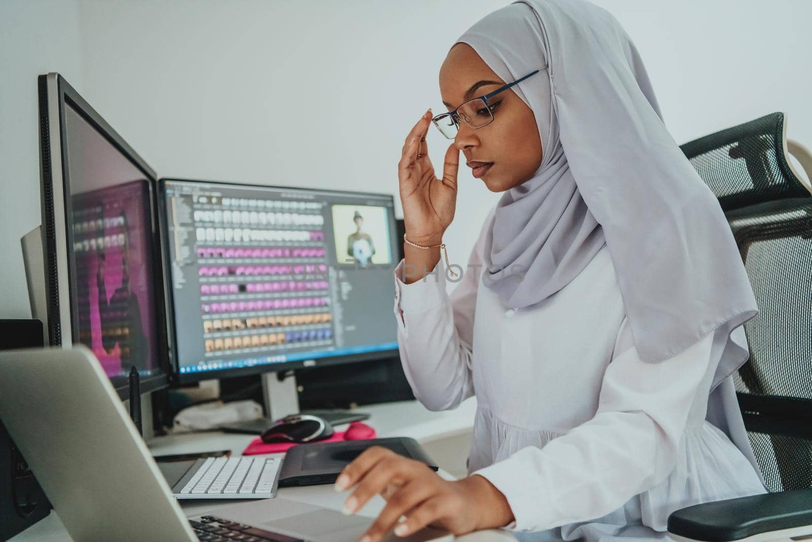 Young Afro-American modern Muslim businesswoman wearing a scarf in a creative bright office workplace with a big screen. High-quality photo