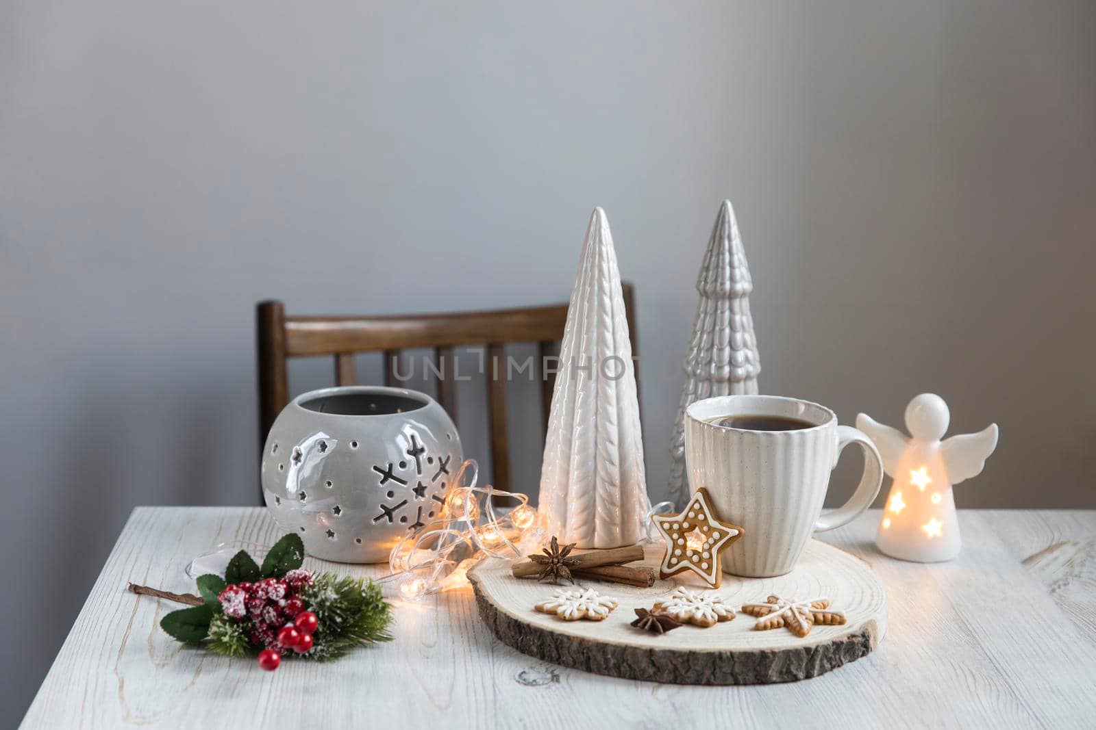 A cup of coffee on a wooden stand, ceramic Christmas trees in pastel colors, gingerbread cookies, gray candlestick. Artificial spruce branch with red berries. Scandinavian style. Copy space. by elenarostunova