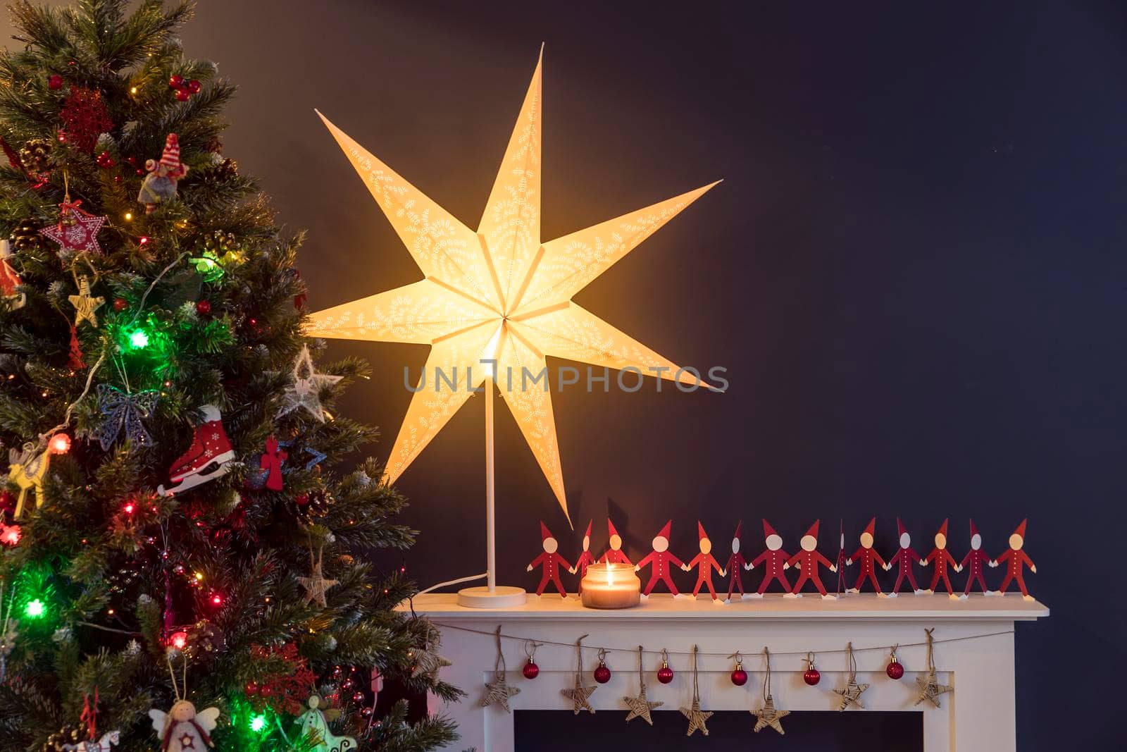 Red paper men holding hands on white and a large paper star on the background of tree there is an artificial fireplace on the background of a dark blue wall as an interior decoration for Christmas