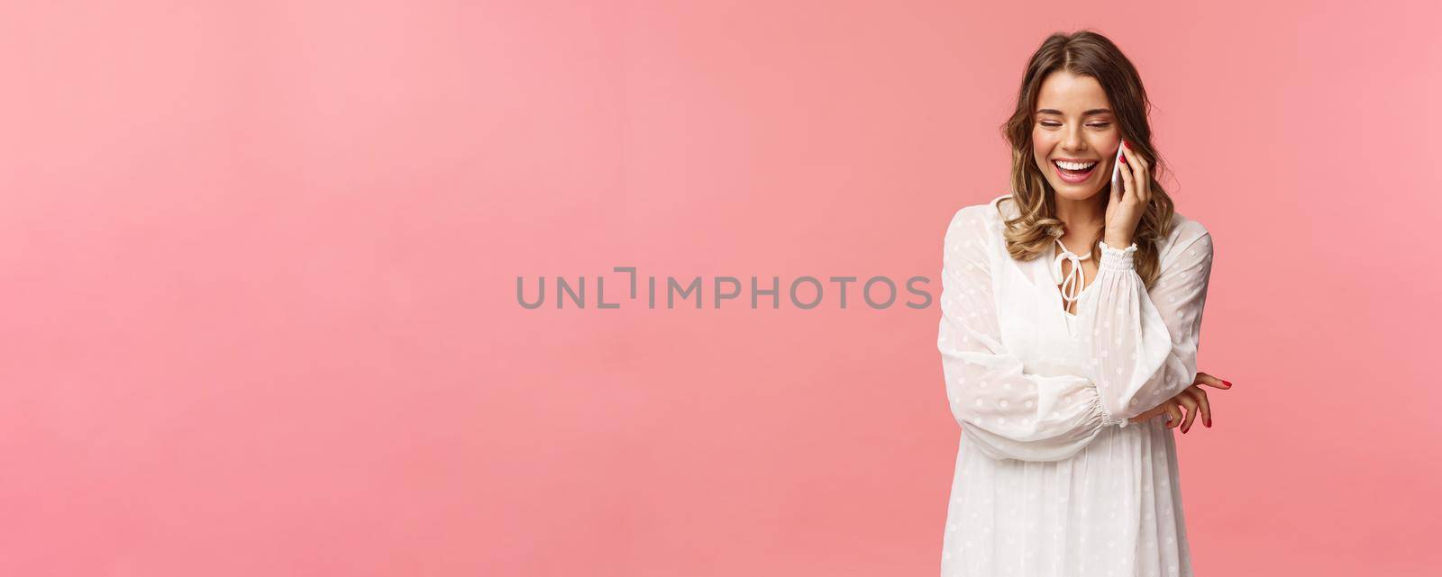 Communication and technology concept. Attractive caucasian female in white dress, blond short haircut, hold smartphone, talking on mobile phone and laughing, smiling carefree, pink background by Benzoix