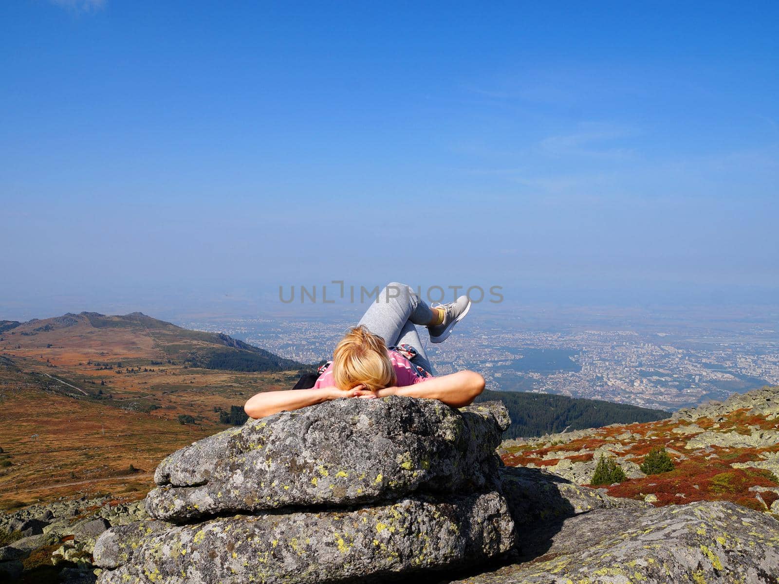 a woman lies on top of a mountain with her legs crossed and looks up at the sky by Annado