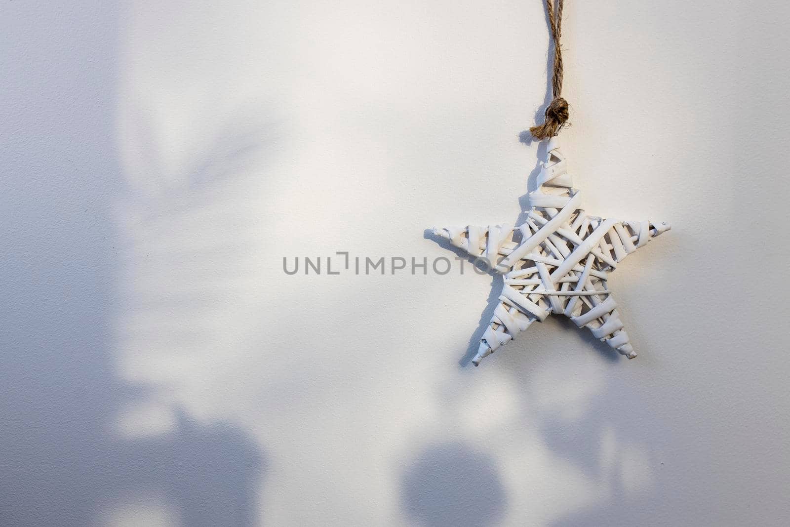 A white wicker willow star hangs on the wall. The shadow from the Christmas tree. Place for text. Copy space