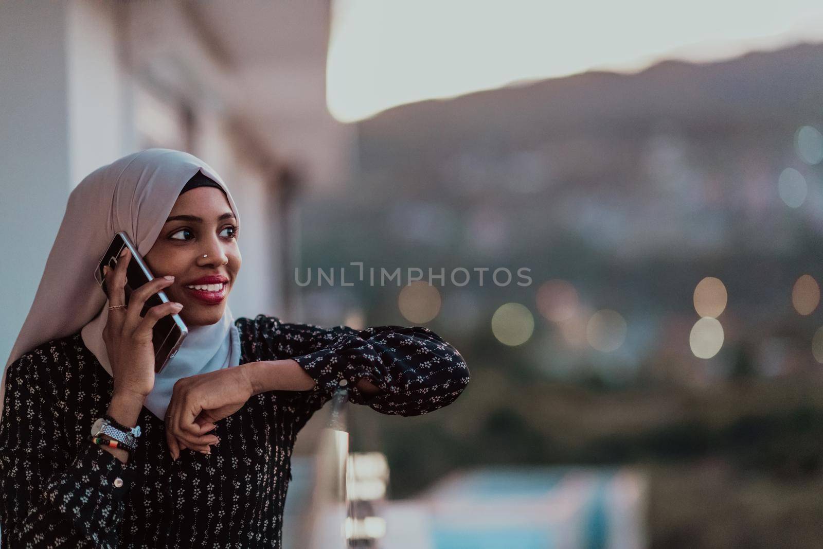 Young Muslim woman wearing scarf veil on urban city street at night texting on a smartphone with bokeh city light in the background. by dotshock