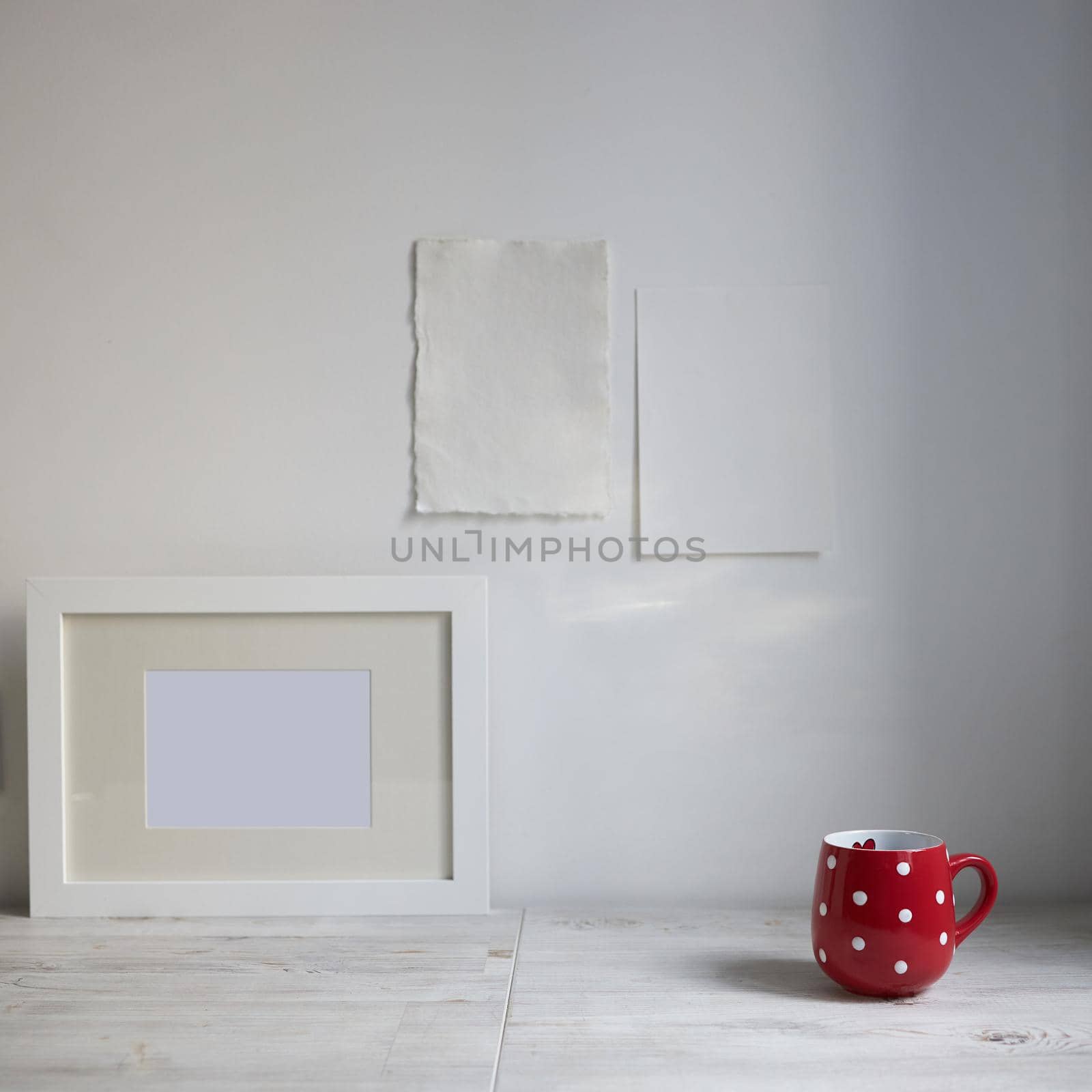 Scandinavian style. Interior Design. A red cup in the dot, a frame for a photo are on the table. Two blank sheets of paper are attached to the wall. Empty space for text by elenarostunova