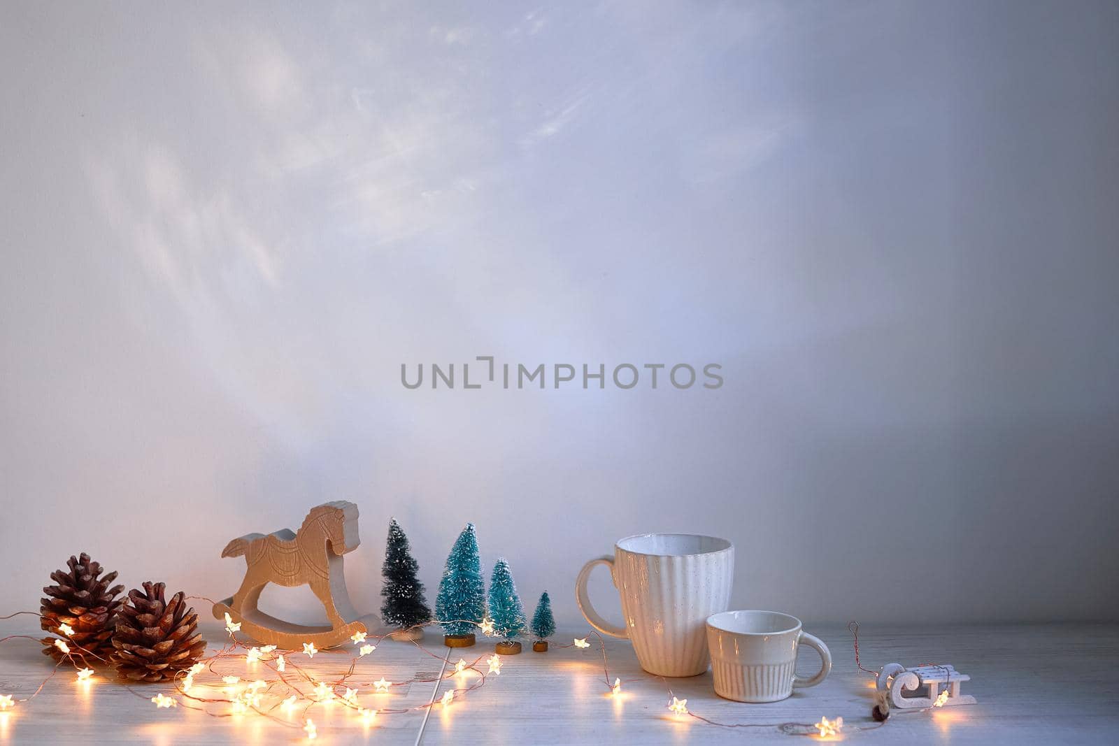 Christmas composition on the table. Wooden gray rocking horse, four small artificial snow-covered trees, angel, garland and mugs