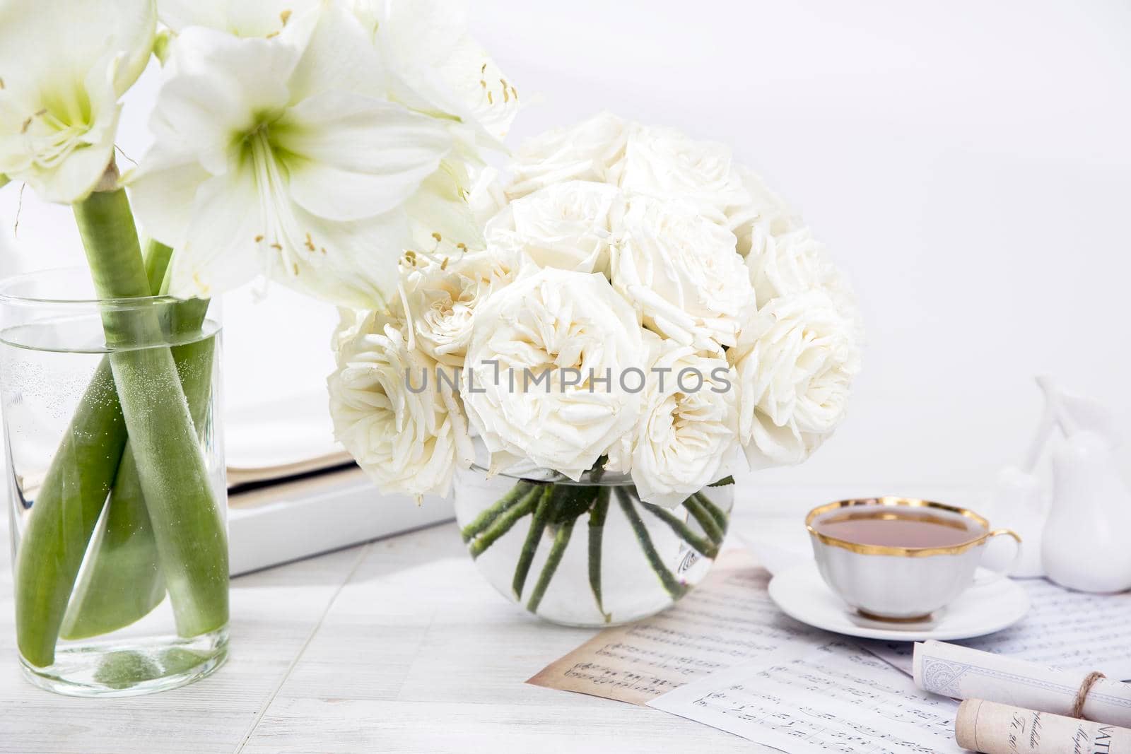 White roses, lily, in round vases with two cups of coffee on the table for a special occasion as a kitchen decoration. Copy space