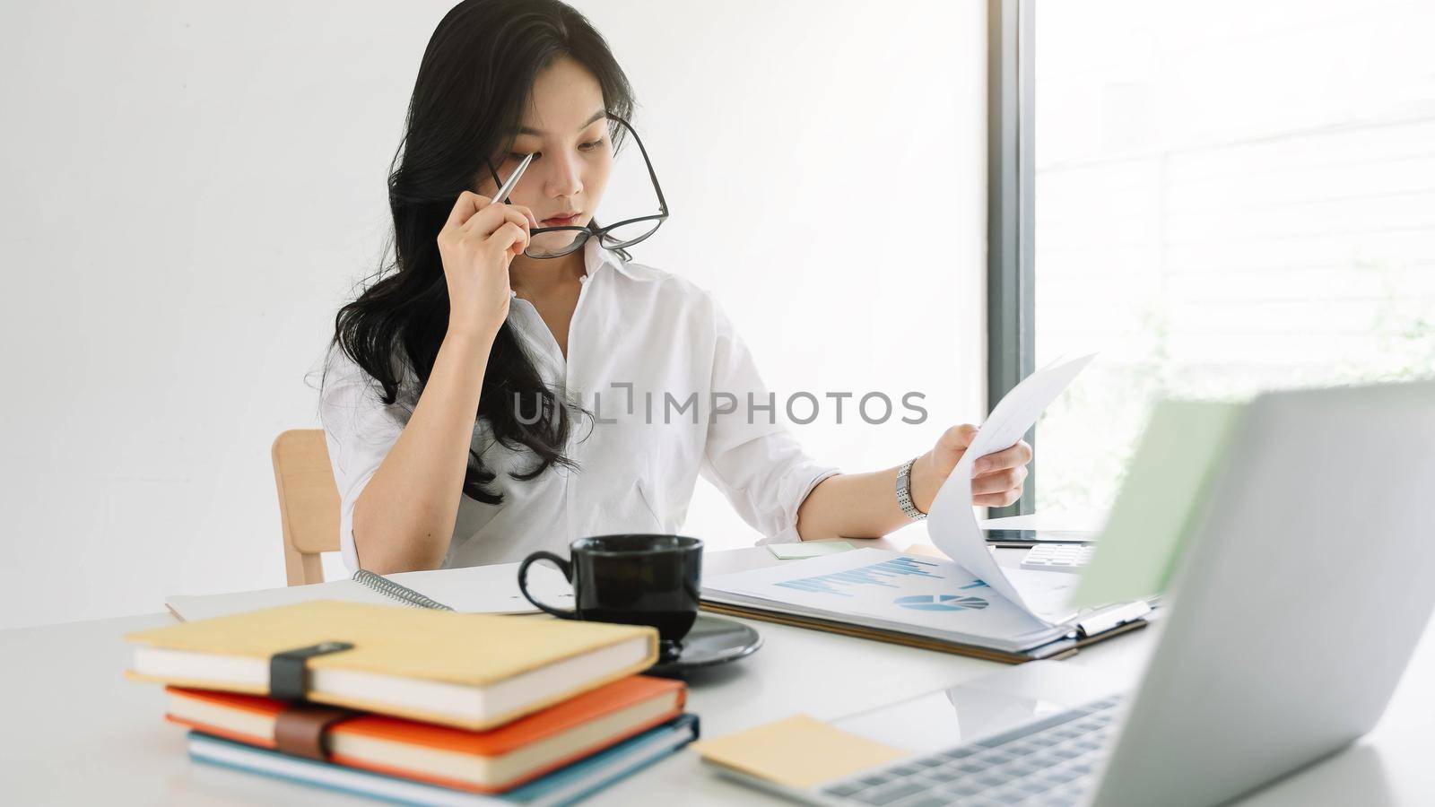 Young asian entrepreneur cogitating thinking making important decision at workplace. Concentrated serious office worker millennial woman analysing results.
