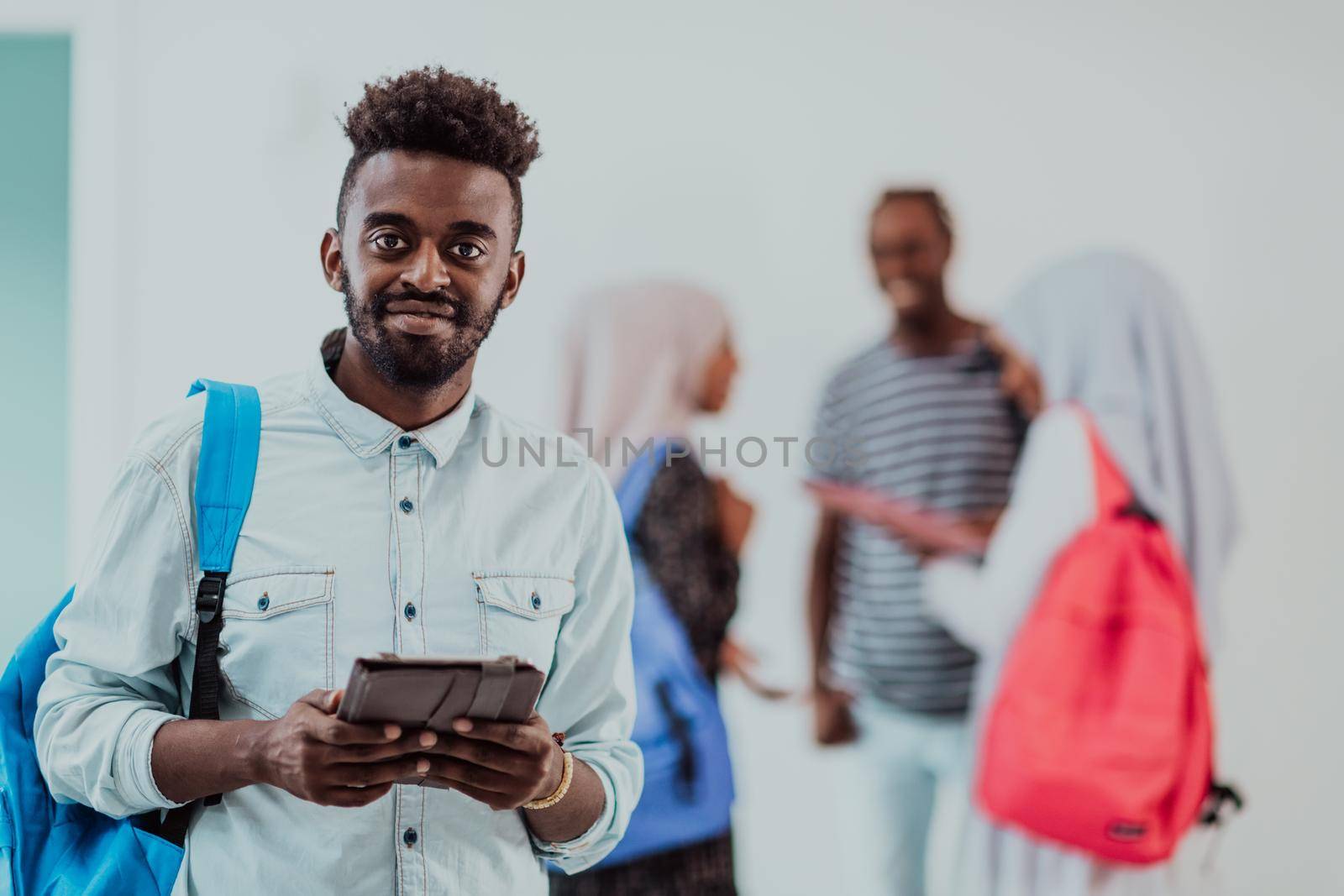 University lifestyle handsome young African student man holding a tablet computer and smiling while standing against university with his friends have a team meeting in the background. High-quality photo by dotshock