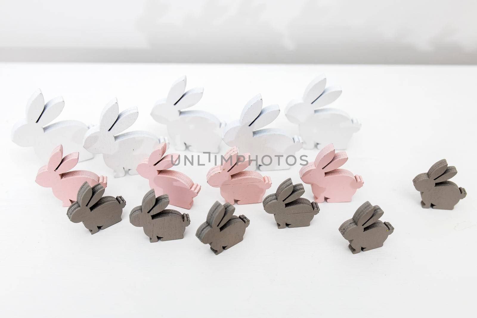 White, gray and pink wooden rabbits of different sizes on a white table surface. Easter decoration. Copy space