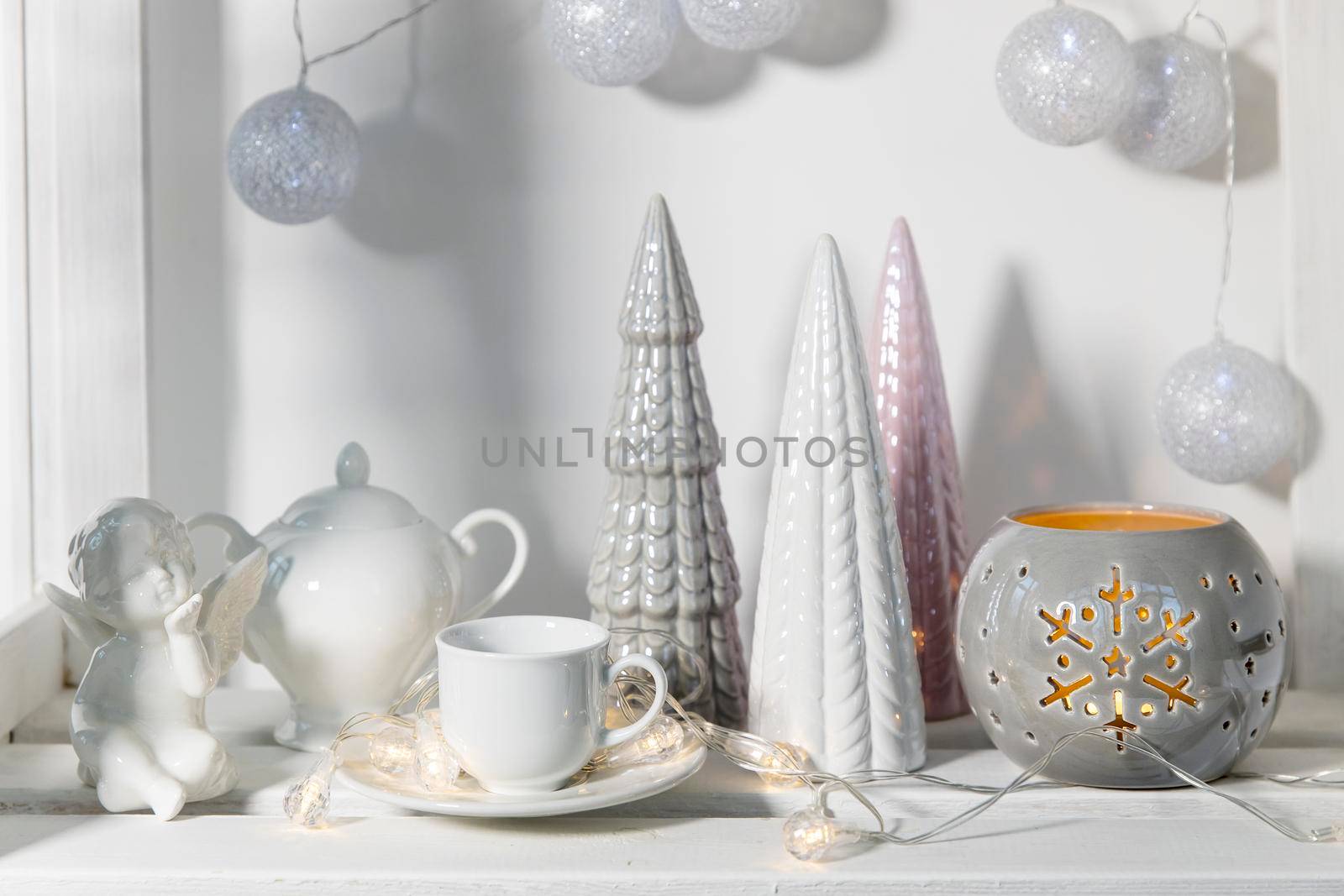 Ceramic figurines of pastel-colored Christmas trees, a white faience angel, a garland of balls made of threads decorate the room before Christmas