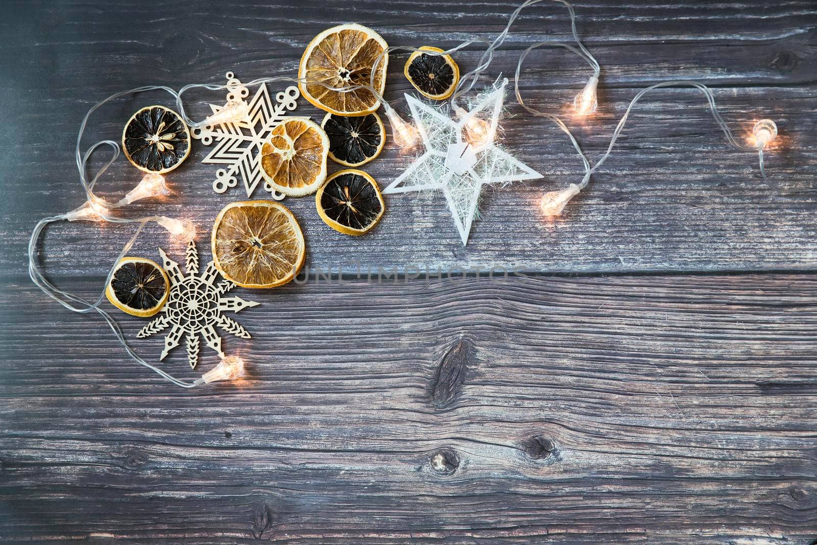 Dried orange slices, thread stars, cut snowflakes, garland on a wooden table. Place for your text. Shooting from above. Copy space by elenarostunova