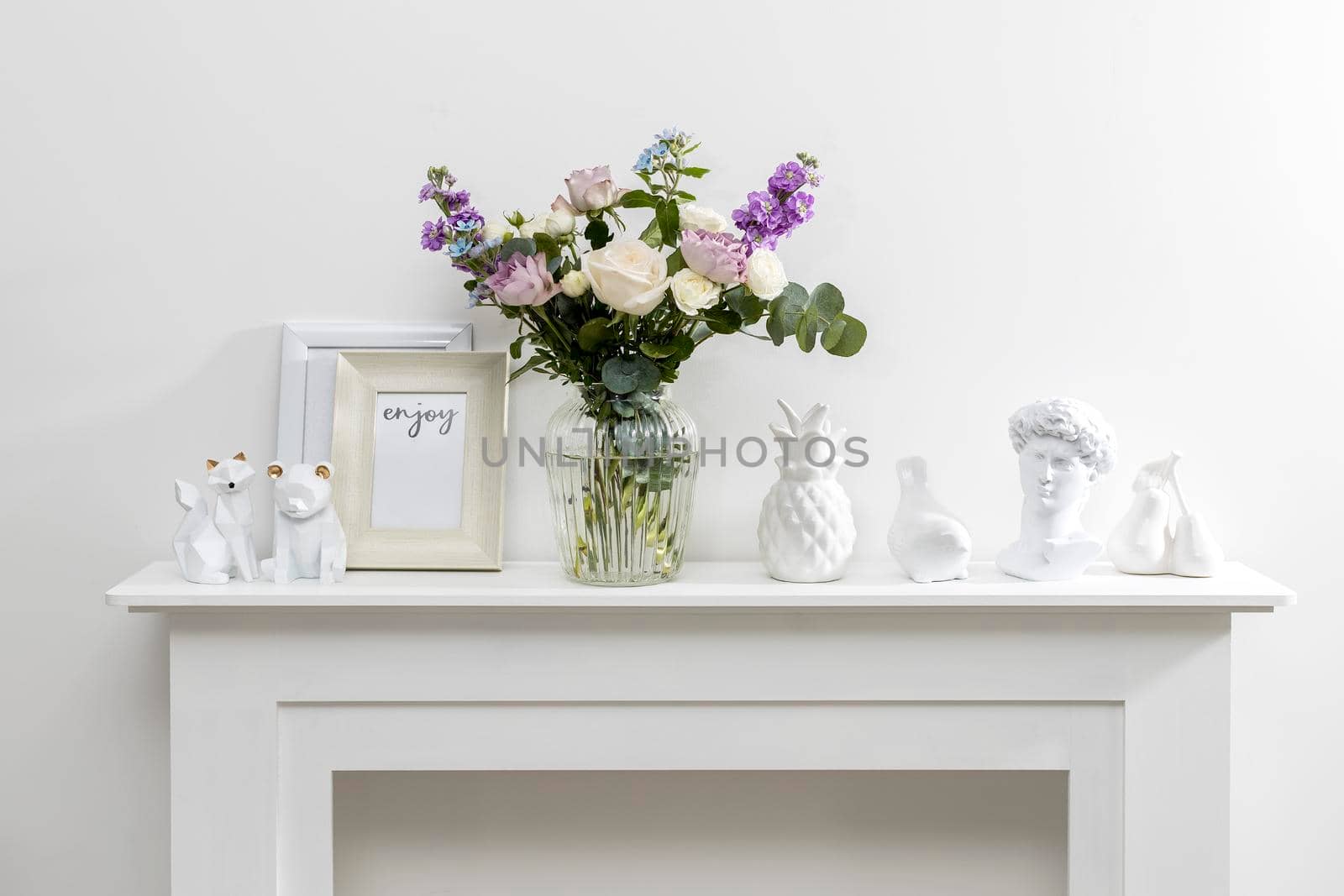 Bouquet of hackelia velutina, purple and white roses, small tea roses, matthiola incana and blue iris in glass vase is on the white coffee table . Grey wall