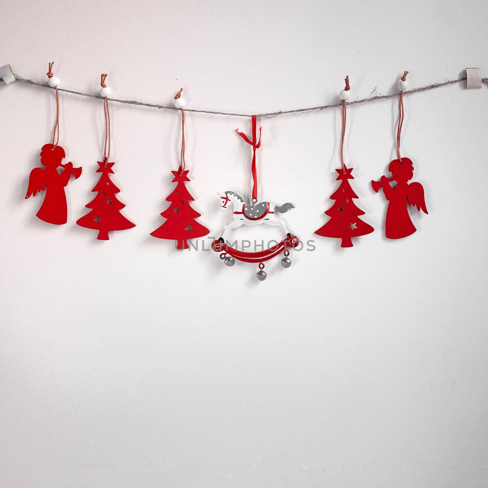 Christmas composition. A garland of red wooden toy fir trees and a rolling horse on a rough rope on a white background. Christmas, winter, new year concept. Flat, top view, copy space by elenarostunova