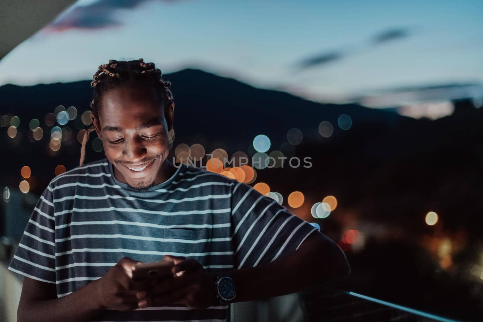 The young man on an urban city street at night texting on smartphone with bokeh and neon city lights in the background. by dotshock
