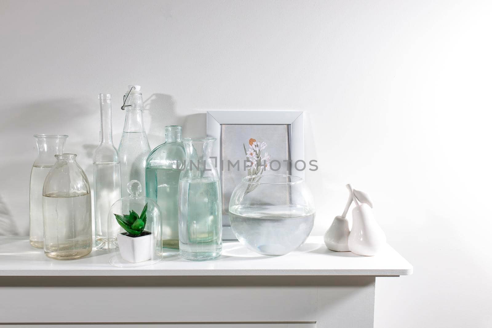 A set of water bottles of different shapes with a photo frame and a pot with artificial succulent is on the dresser. Copy space