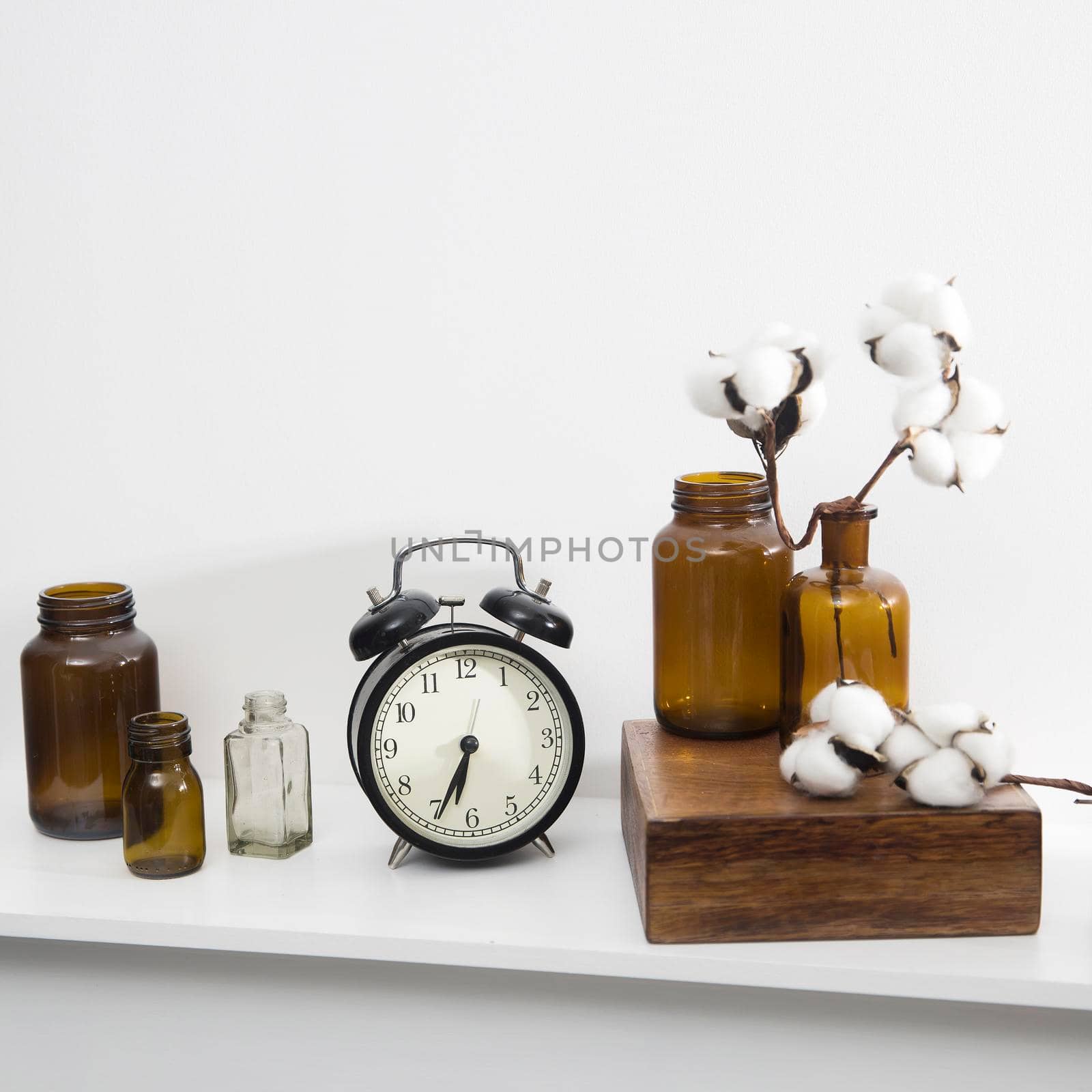 Cotton flowers in glass brown small pharmaceutical bottles on white table surface as room decoration. The clock shows six.