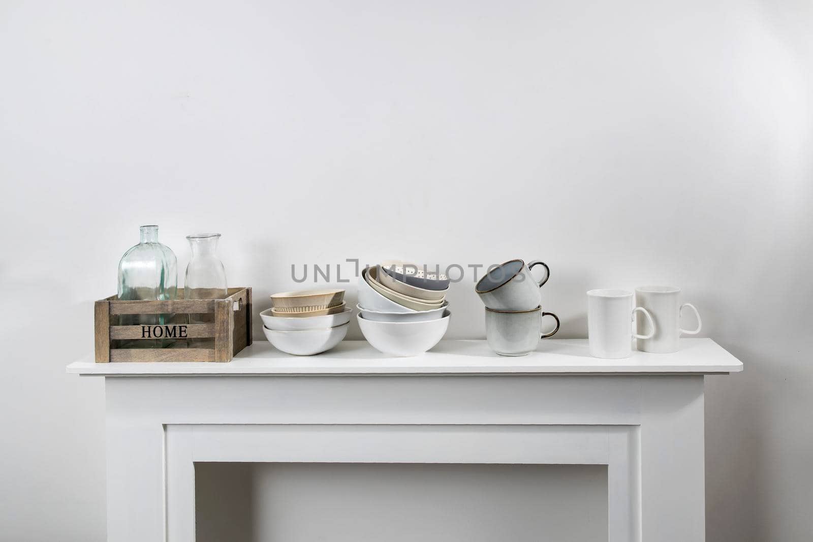 kitchen utensils, cups, bowls, bottles, storage items, artificial monstera in a ceramic pot are on a white dresser by elenarostunova