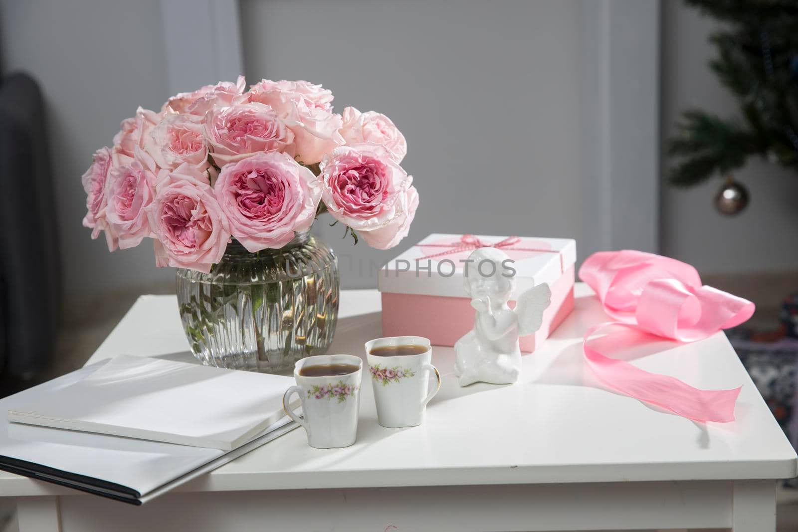 Rose White Pink O'hara. a bouquet of pink roses in vase, two porcelain cups with tea, box with heart with gift, satin ribbon, figurine of angel - gifts for Valentine's Day on coffee table.