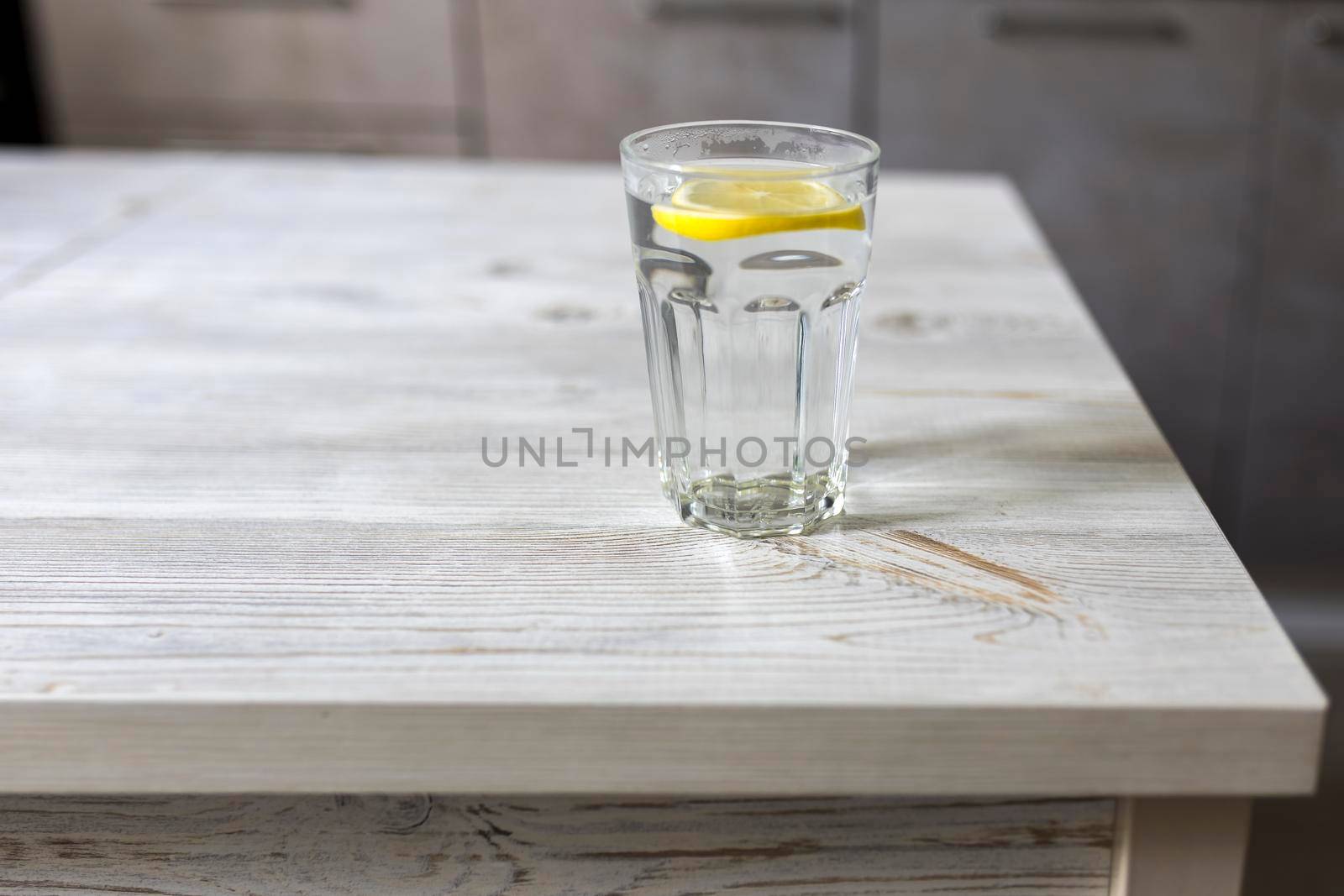 Transparent glass tables with a slice of lemon are on a wooden table in a beige kitchen interior. Empty space by elenarostunova